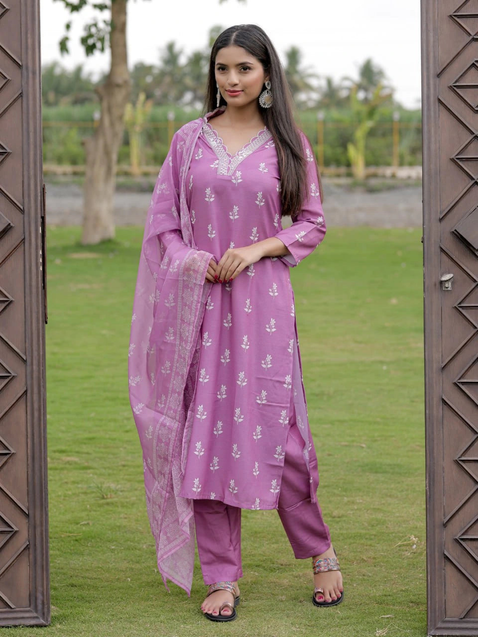 Woman in a pink traditional outfit standing in a grassy area with trees in the background